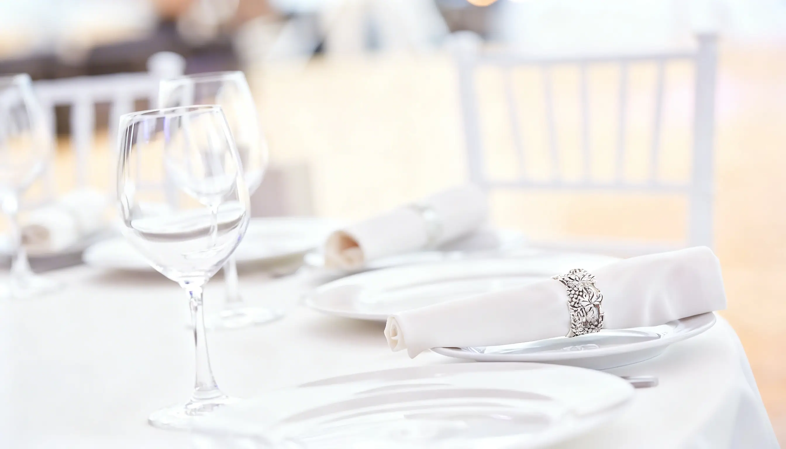 Elegant dining setup with crystal glasses, white plates, and neatly rolled napkins adorned with silver rings.